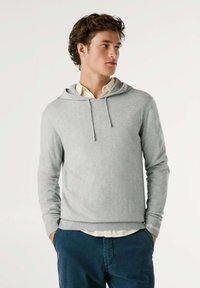 Lichtgrijze hoodie van zacht materiaal, met een trekkoord, lange mouwen, ribgebreide manchetten en een relaxed fit over een overhemd met kraag.