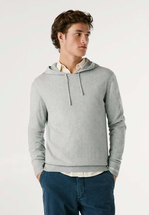 Lichtgrijze hoodie van zacht materiaal, met een trekkoord, lange mouwen, ribgebreide manchetten en een relaxed fit over een overhemd met kraag.