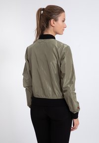 Olivgrüne Bomberjacke mit glatter Oberfläche, geripptem schwarzen Kragen und Bündchen, taillierter Passform und kleinem Logo auf dem Ärmel.