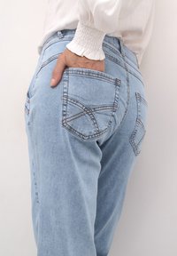 Jeans in denim azzurro chiaro con una texture liscia, dotati di due tasche posteriori e cuciture decorative. La vita presenta un design arricciato.