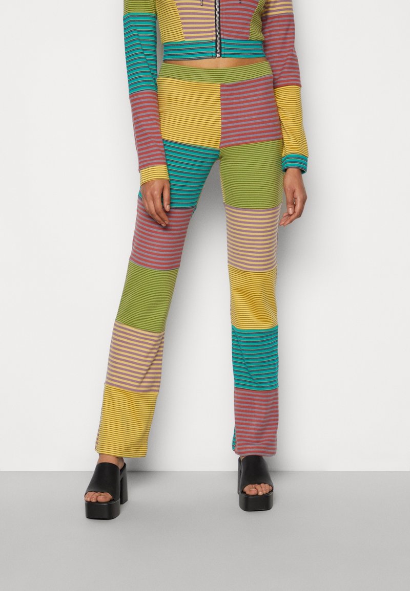 Tenue en patchwork coloré avec des rayures horizontales ; les matériaux comprennent un tissu extensible. Comprend une veste zippée courte et un pantalon évasé.
