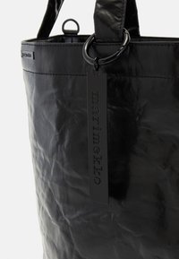 Black leather handbag with a textured finish. Features a sturdy handle, circular hardware, and a branded black tag attached.