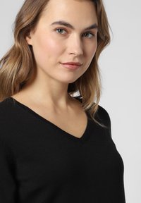 Schwarzer V-Ausschnitt-Pullover aus weichem Material mit glatter Textur und taillierter Passform, hervorgehoben gegen einen neutralen Hintergrund.