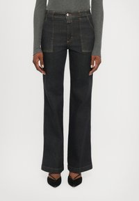 Jean large en denim foncé à taille haute, avec des coutures contrastantes, une fermeture par bouton et un ourlet net. Assorti à des talons noirs.