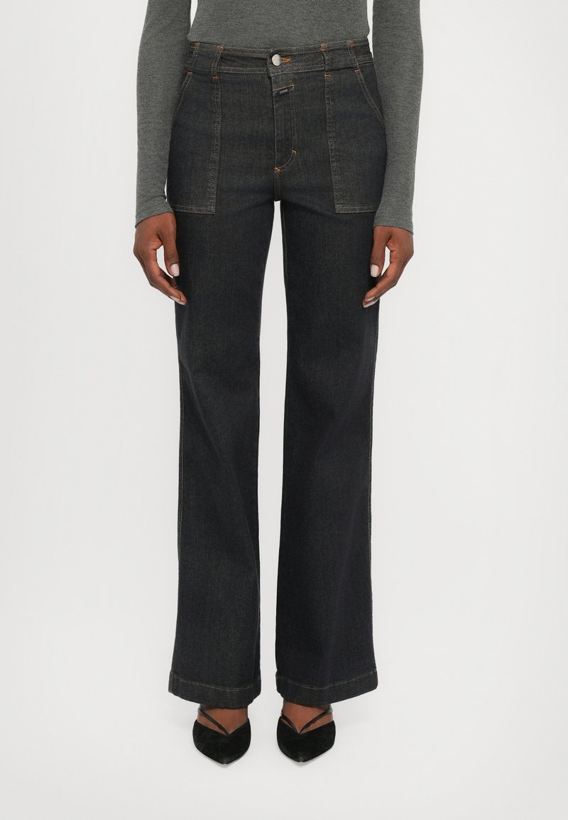 Jean large en denim foncé à taille haute, avec des coutures contrastantes, une fermeture par bouton et un ourlet net. Assorti à des talons noirs.