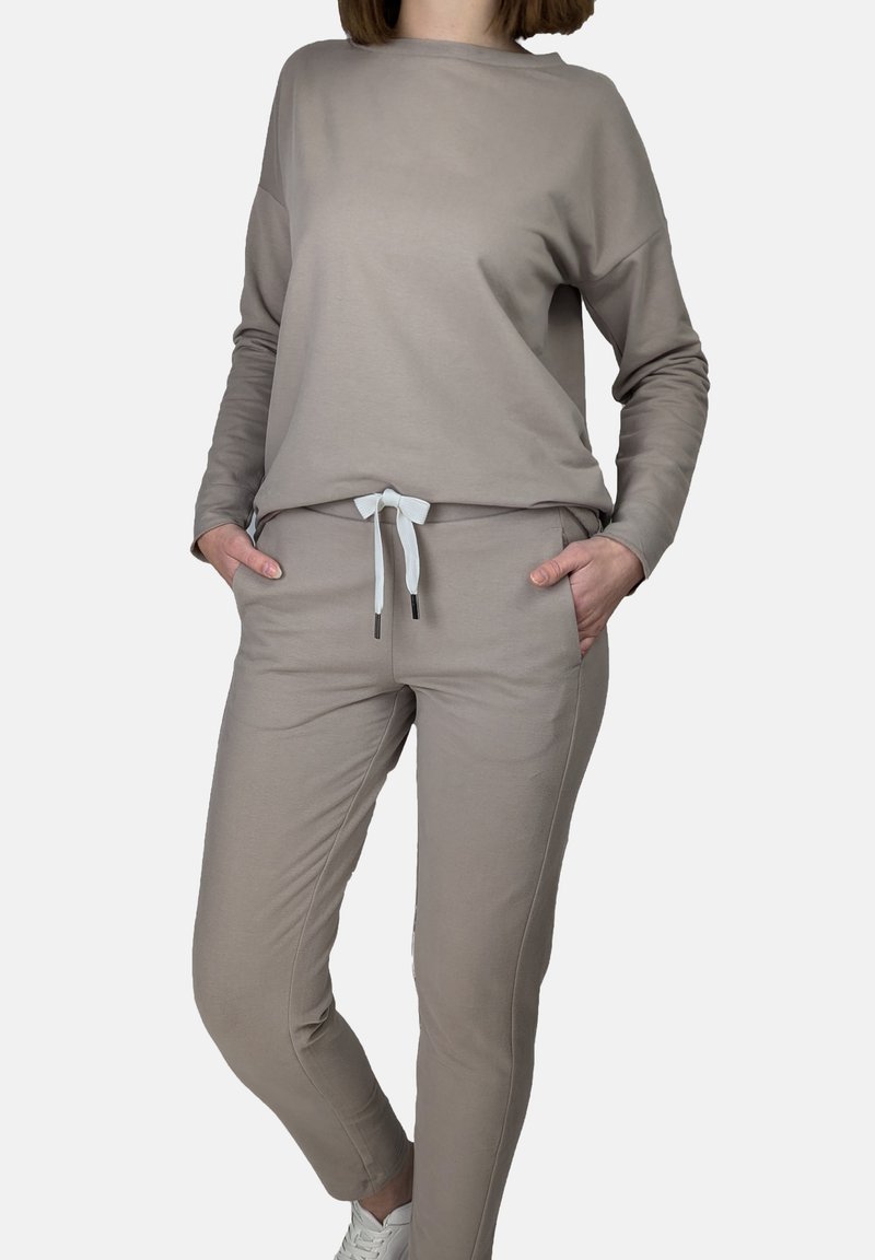 Beiges Loungewear-Set aus weichem Stoff. Besteht aus einem lässigen Langarmoberteil und tapered Hosen mit Kordelzug und Seitentaschen.
