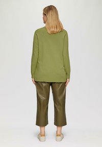 Groene gebreide trui met lange mouwen en een relaxte pasvorm, gecombineerd met olijfgroene faux leren broeken, die op de kuit zijn afgeknipt.