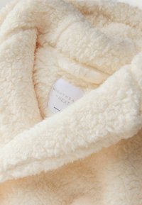Cremefarbener, flauschiger Nachtwäschestoff mit strukturierter Oberfläche. Verfügt über ein Etikett mit "NACHTWÄSCHE von NEXT." Weiche und einladende Optik.