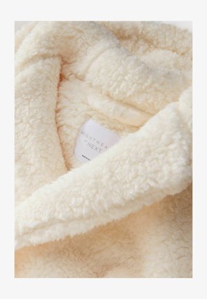 Tessuto da notte di colore crema, morbido e fluffy, con una superficie texturizzata. Presenta un'etichetta con "NIGHTWEAR by NEXT." Aspetto morbido e invitante.