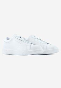 Zapatillas de cuero blanco con punteras redondeadas, cordones planos y suelas de goma texturizada, que presentan un diseño minimalista y un acabado suave.
