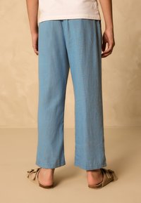 Pantalon bleu clair à jambes larges avec une ceinture élastique, présentant une texture lisse et un ourlet légèrement retroussé.