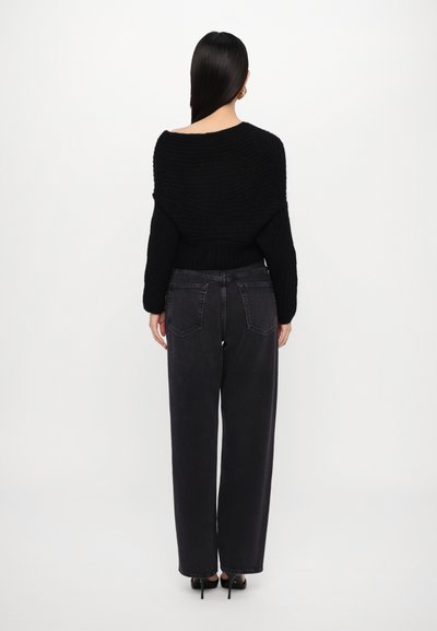 Black knitted sweater with a wide, off-the-shoulder neckline, paired with black high-waisted wide-leg jeans and high-heeled shoes.