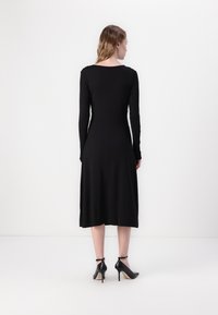 Black, long-sleeve dress with a fitted bodice and A-line skirt. Smooth, stretchy fabric. Paired with black high-heel shoes.