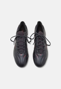 Crne sportske cipele s gornjištem od sintetičke kože, teksturiranim mrežastim jezikom, crvenim akcentima i ravnim vezicama. Elegantan, aerodinamičan dizajn.