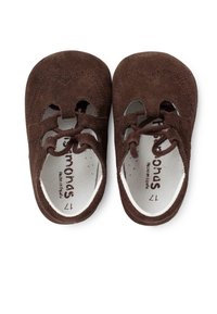 Scarpe in suede marrone con punta rotonda, caratterizzate da dettagli intagliati e chiusura con lacci. L'interno presenta una fodera bianca con un dettaglio del logo stampato.