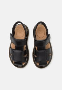 Sandali in pelle nera con design aperto, cinturini regolabili in velcro, soletta imbottita marrone e cuciture gialle lungo la suola.