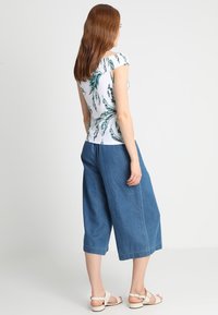 Bílý top s zeleným vzorem listů, krátké rukávy, kombinovaný s širokými džínovými culottes v modré barvě. Sandály s nastavovacími popruhy.