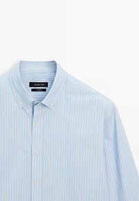Camicia azzurra a righe con colletto, caratterizzata da sottili linee verticali bianche, rosse e gialle. Il tessuto appare liscio e intrecciato.
