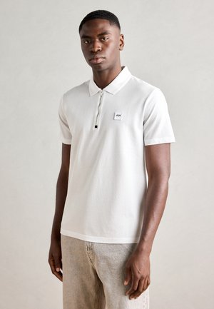 White polo shirt with short sleeves, featuring a zip placket and a small logo patch on the chest. Made of smooth, lightweight fabric.