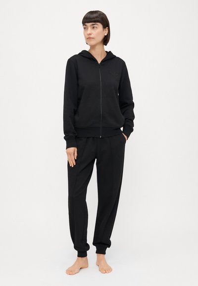 Crna zip-up dukserica s kenguruznim džepom i rebrastim manžetama, u kombinaciji s odgovarajućim tapered trenirkama s utisnutim logotipom.