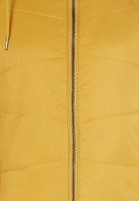 Gelbe gepolsterte Jacke mit einem Reißverschluss an der Vorderseite. Sie hat eine glatte Textur und ein horizontales Steppmuster. Enthält einen Kordelzug an der Kapuze.
