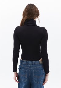 Schwarzer Langarm-Rollkragenbody mit glatter Textur. Kombiniert mit hochgeschnittenen blauen Jeans mit zwei Gesäßtaschen.