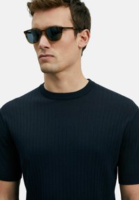 Marineblauwe geribbelde korte mouw trui met een ronde halslijn, met een gladde textuur en een aansluitend ontwerp. Verbonden met donkere zonnebril.