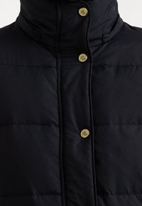 Námořnická puffer vesta s vysokým límcem, která má zlaté knoflíky s logem "RL", prošívanou texturu a elegantní, přiléhavý design.