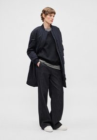 Námornícka bomber bunda cez čiernu mikinu s prúžkovaným lemom, skombinovaná s voľnými tmavými džínsami a bielymi teniskami. Jednoduchý, čistý dizajn.