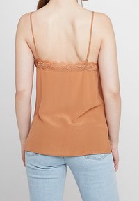 Kanelfarvet cami-top med blondedetalje ved halsudskæringen, tynde justerbare stropper og en blød, glat tekstur, parret med lyseblå jeans.