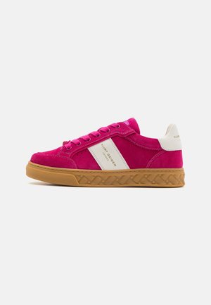 Zapatilla baja rosa de ante con franja lateral beige y lengüeta en el talón, suela de goma y cierre de cordones, con la marca "Kurt Geiger London" en el lateral.