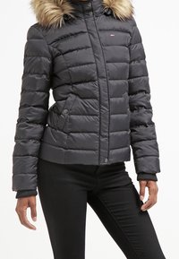 Polstrovaná černá bunda s umělou kožešinou na kapuci, s horizontálním prošíváním, zipovým zapínáním a bočními kapsami. Elegantní žebrované manžety.
