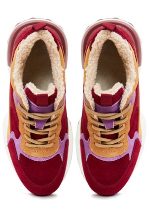 Des baskets en suède rouge et beige avec une doublure en peluche beige, des accents violets et des lacets marron. Elles présentent une semelle blanche épaisse et une languette à l'arrière.