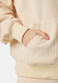 Felpa a righe crema con cappuccio, dotata di tasca a marsupio, polsini elasticizzati e una texture morbida, che presenta sottili linee verticali.