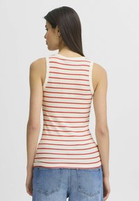 Débardeur crème avec des rayures horizontales rouges, design ajusté, texture côtelée et bretelles larges. Porté avec un short en denim bleu clair.