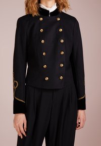 Černá zkrácená bunda z vlny se zlatými knoflíky a sametovými doplňky, zdobená propracovanou zlatou výšivkou na rukávech.