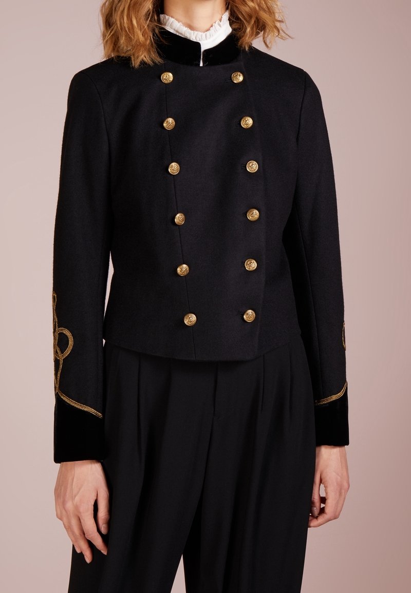 Černá zkrácená bunda z vlny se zlatými knoflíky a sametovými doplňky, zdobená propracovanou zlatou výšivkou na rukávech.