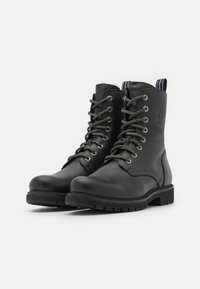 Bottes noires en cuir jusqu'à la cheville avec bout rond, lacets à l'avant et œillets métalliques. Semelle texturée noire et tirant à l'arrière.