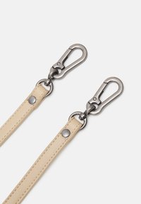 Beżowe skórzane paski z srebrnymi metalowymi zaczepami obrotowymi i nitami na białym tle, pokazane z bliska.