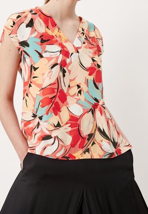 Haut sans manches à col en V avec un imprimé floral abstrait rouge vif, pêche, bleu et noir, porté avec un pantalon noir.