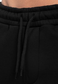 Schwarze Sweatpants mit einem dicken elastischen Bund und Kordelzug, Seitentaschen und einer glatten Textur.