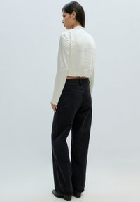 Witte langekorte top en hoge zwarte wijdgevormde jeans met een gestructureerde afwerking en elastische tailleband, gezien van achteren.