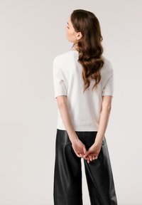 Weißes Kurzarmoberteil mit lässiger Passform, kombiniert mit schwarzen Leder-Hose im weiten Schnitt. Glatte Textur, minimalistisches Design.