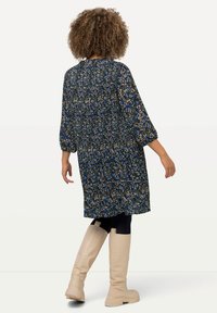 Floral-patterned black dress with long sleeves, gathered waist, and knee-length cut. Paired with beige knee-high boots and black leggings.