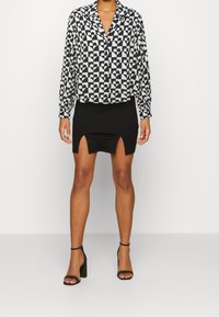 Chemise à manches longues noire et blanche à motifs de cœurs, associée à une mini-jupe noire avec deux fentes à l'avant et des sandales noires à talons blocs.