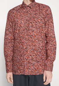 Camicia a maniche lunghe con un motivo floreale rosso, nero e bianco, design con bottoni e colletto a punta, realizzata in un tessuto leggero.