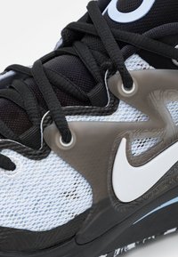 Czarno-niebieski but sportowy z siateczkową cholewką, dużym białym logo Swoosh, skomplikowanym wzorem podeszwy i trwałymi sznurówkami zapewniającymi pewne dopasowanie.