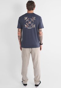 T-shirt en coton bleu marine avec un design floral multicolore au dos, associé à un pantalon en velours côtelé beige clair et des chaussures noires.