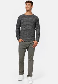 Szara koszula z długim rękawem w teksturowane poziome paski, zestawiona z jasnoszarymi spodniami slim fit i białymi trampkami. Model przyjmuje neutralną pozę.