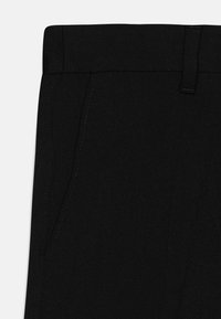 Pantalon noir avec une texture de tissu lisse, une taille plate et des poches latérales avec des détails de couture subtils.